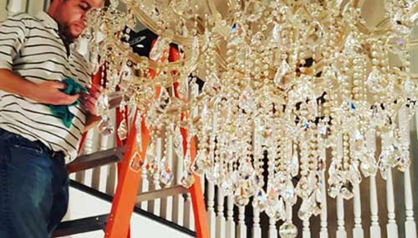 A man standing on a ladder near a chandelier.